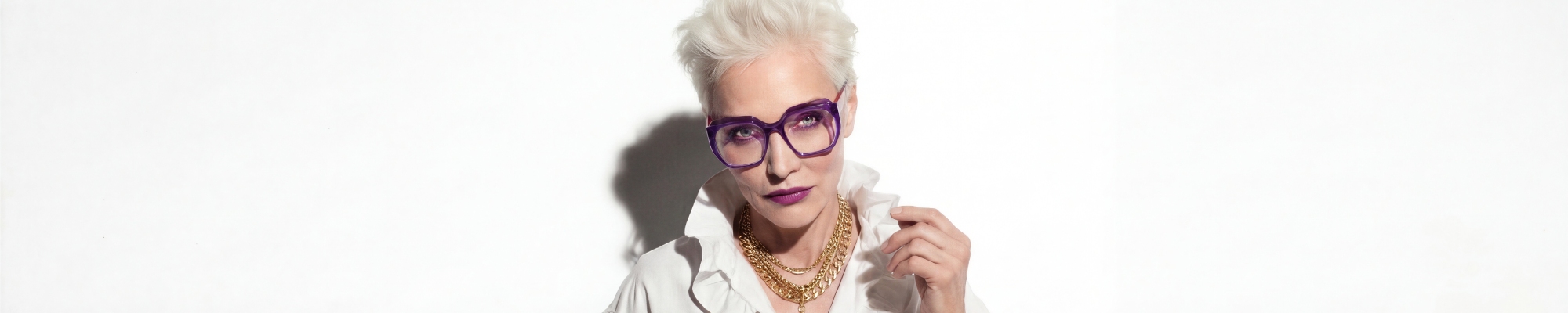 Femme aux cheveux blancs portant des lunettes de vue design violettes.